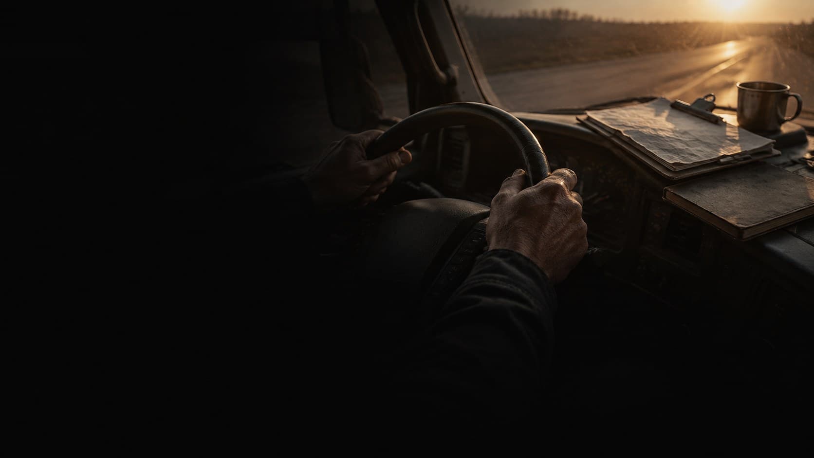 A driver's hands on the wheel at dawn, paperwork on the dash