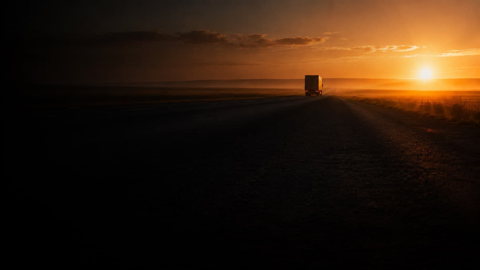 A semi-truck on an open highway at sunrise